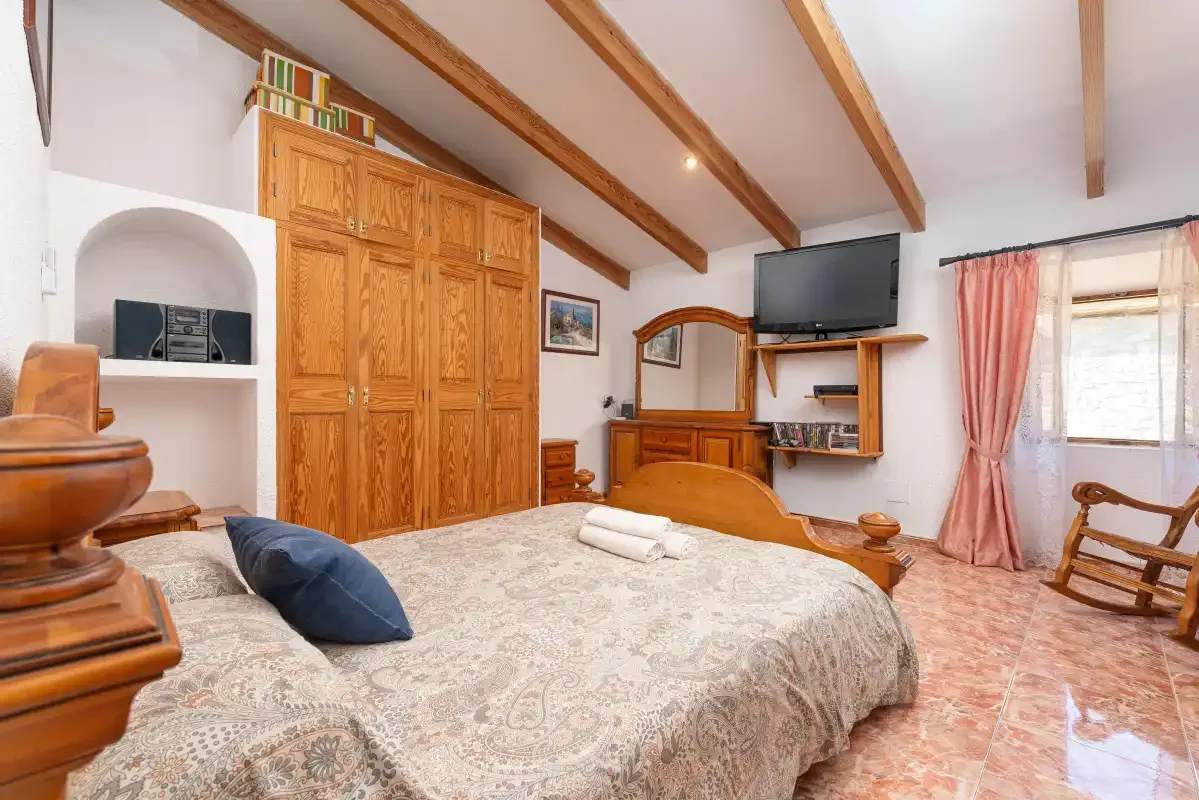 A bedroom with a large bed, wooden wardrobe, and television.