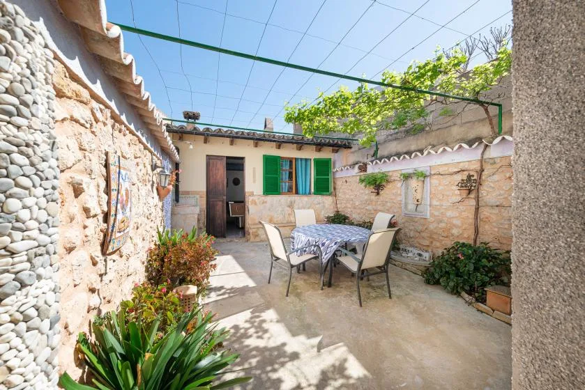 A stone courtyard with an outdoor table and chairs beneath a vine-covered trellis.
