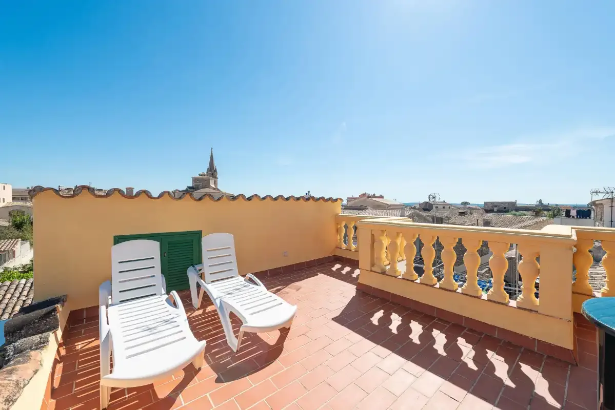 A sunny rooftop terrace with white loungers and a view of nearby buildings.