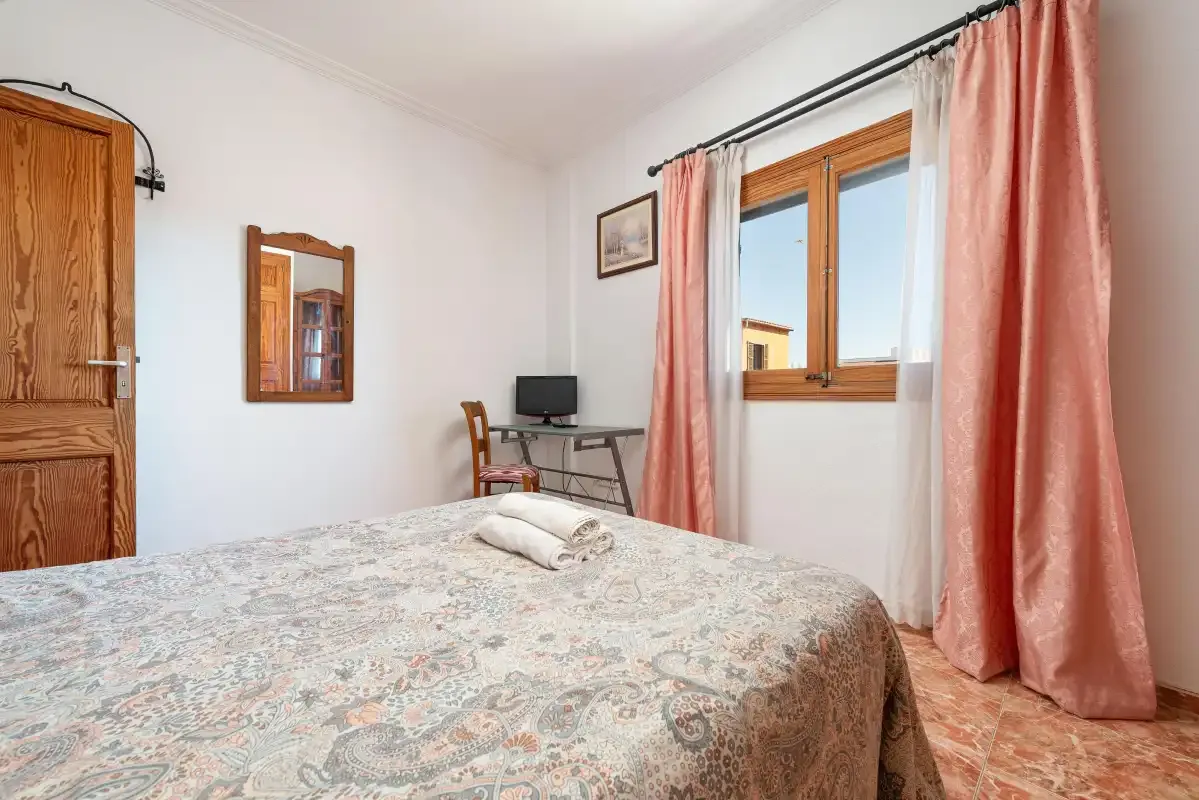 A bedroom with a patterned bedspread, window, and pink curtains.