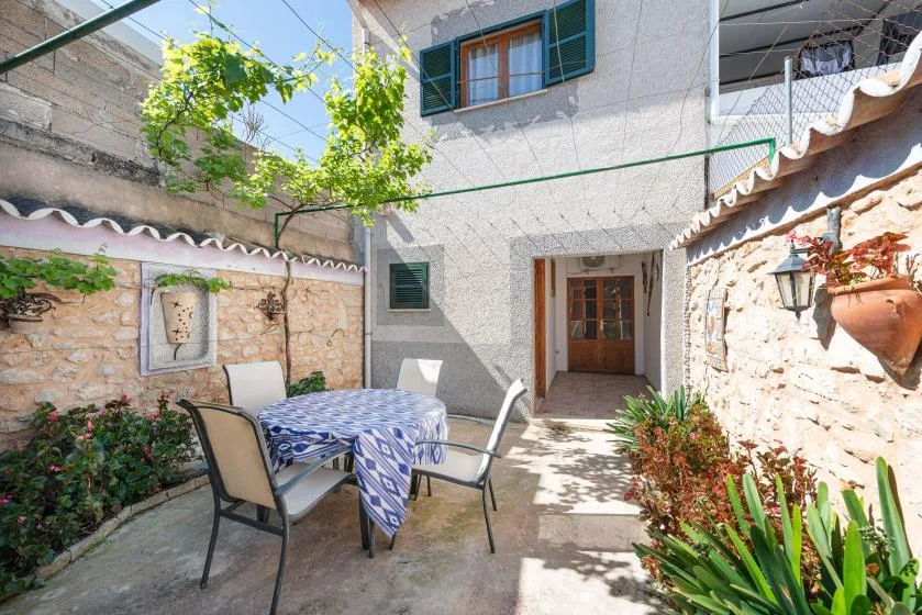 A sunny stone courtyard with a dining table, seating, and a doorway.