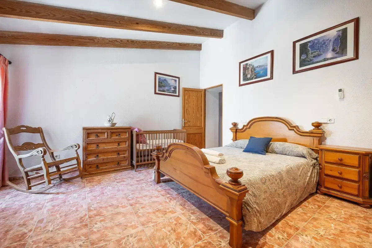 A bedroom with a wooden bed, dresser, and exposed ceiling beams.