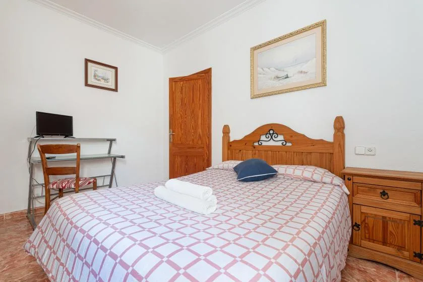 A bedroom with a patterned bedspread, wooden headboard, desk, and television.