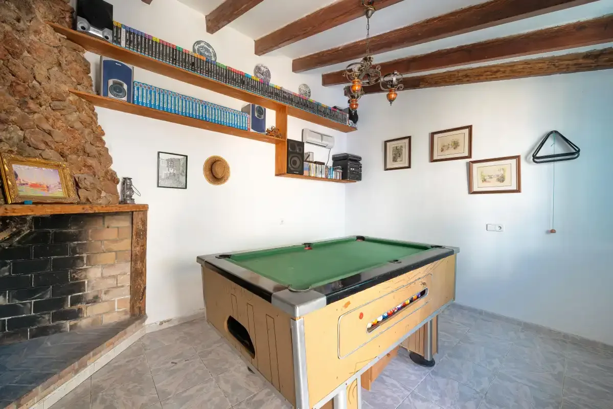 A billiards room with a green-felt pool table and a stone fireplace.