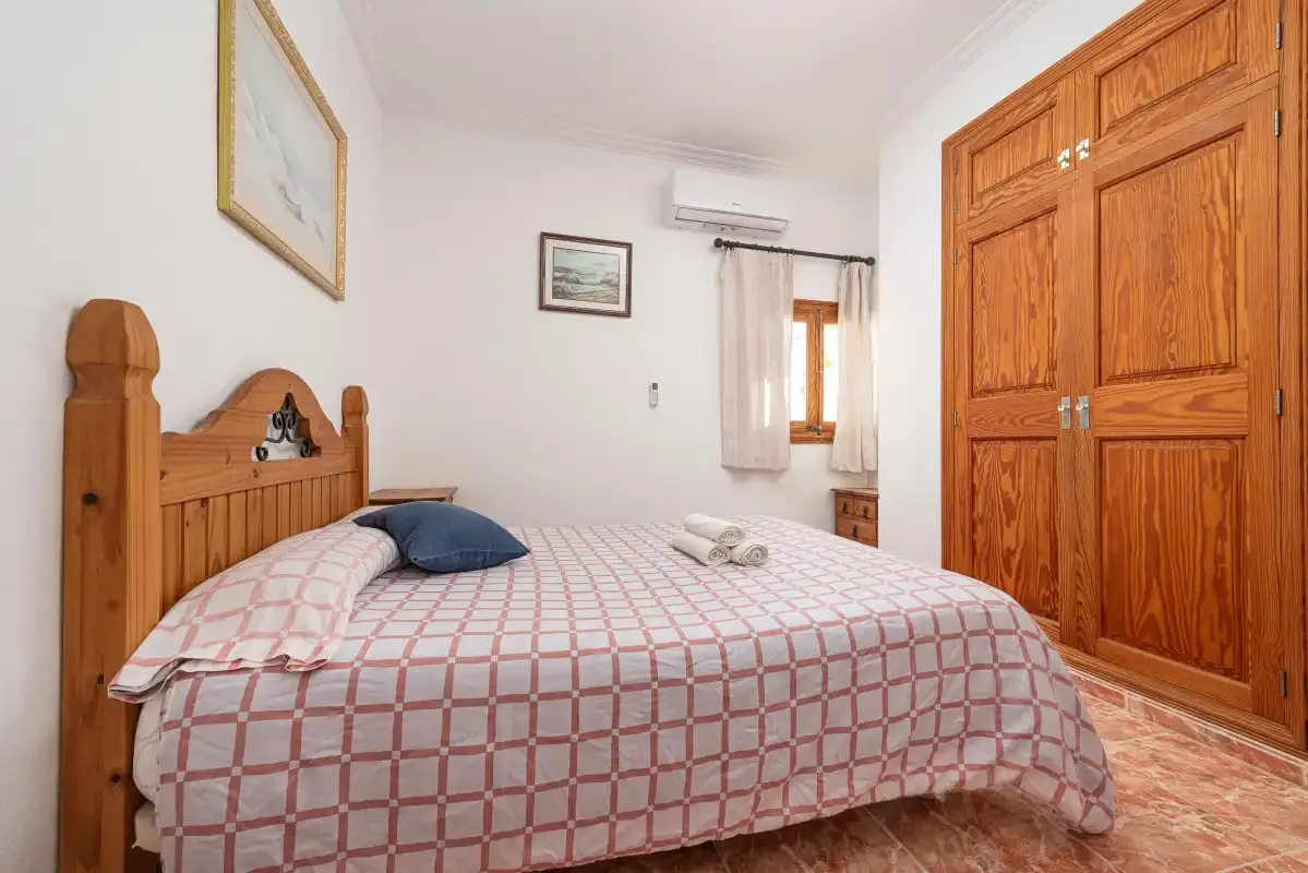 A bedroom with a bed, wooden wardrobe, and a small window.