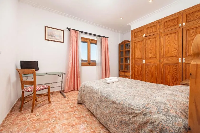 A bedroom with a bed, wooden wardrobes, and a curtained window.