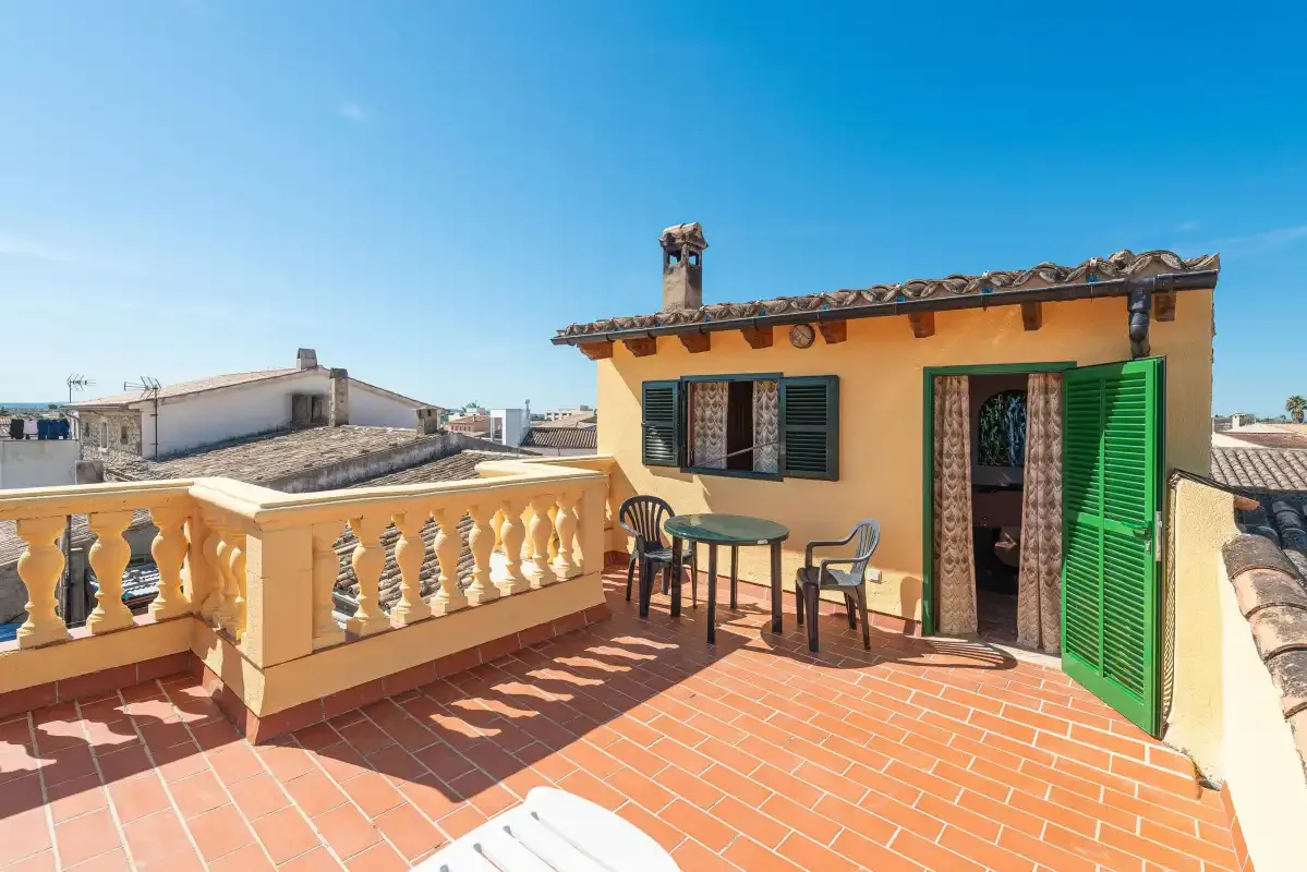 A sunny rooftop terrace with a small table and chairs beside a yellow building.