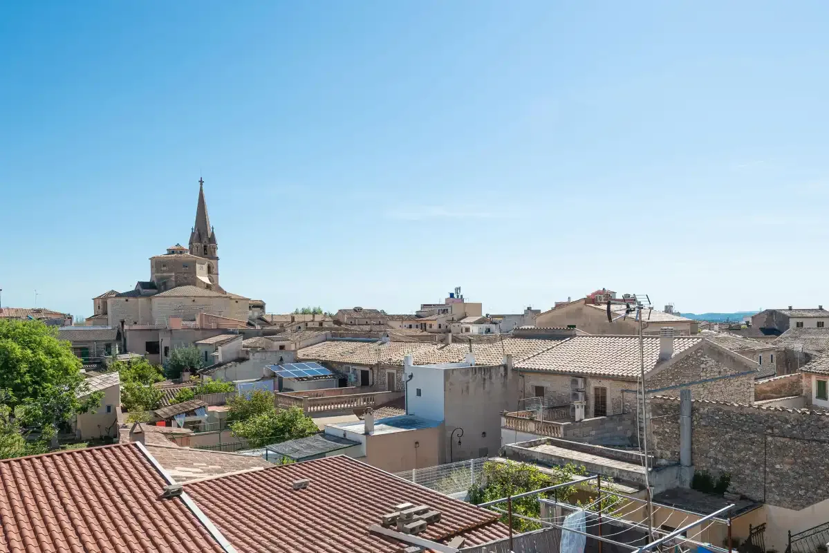 A village townscape of tiled rooftops and buildings beneath a clear blue sky.