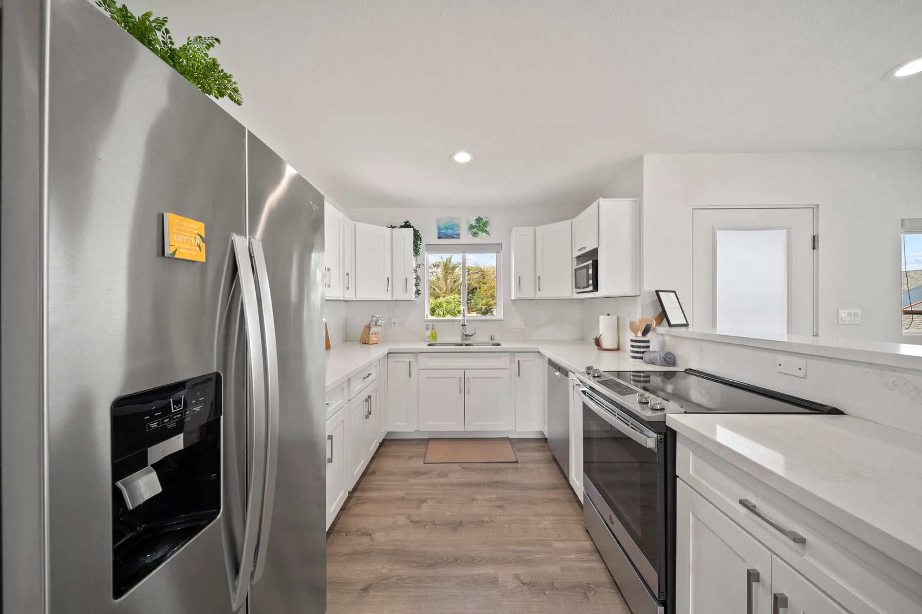 Una cocina luminosa con gabinetes blancos, electrodomésticos de acero inoxidable y piso de aspecto madera.