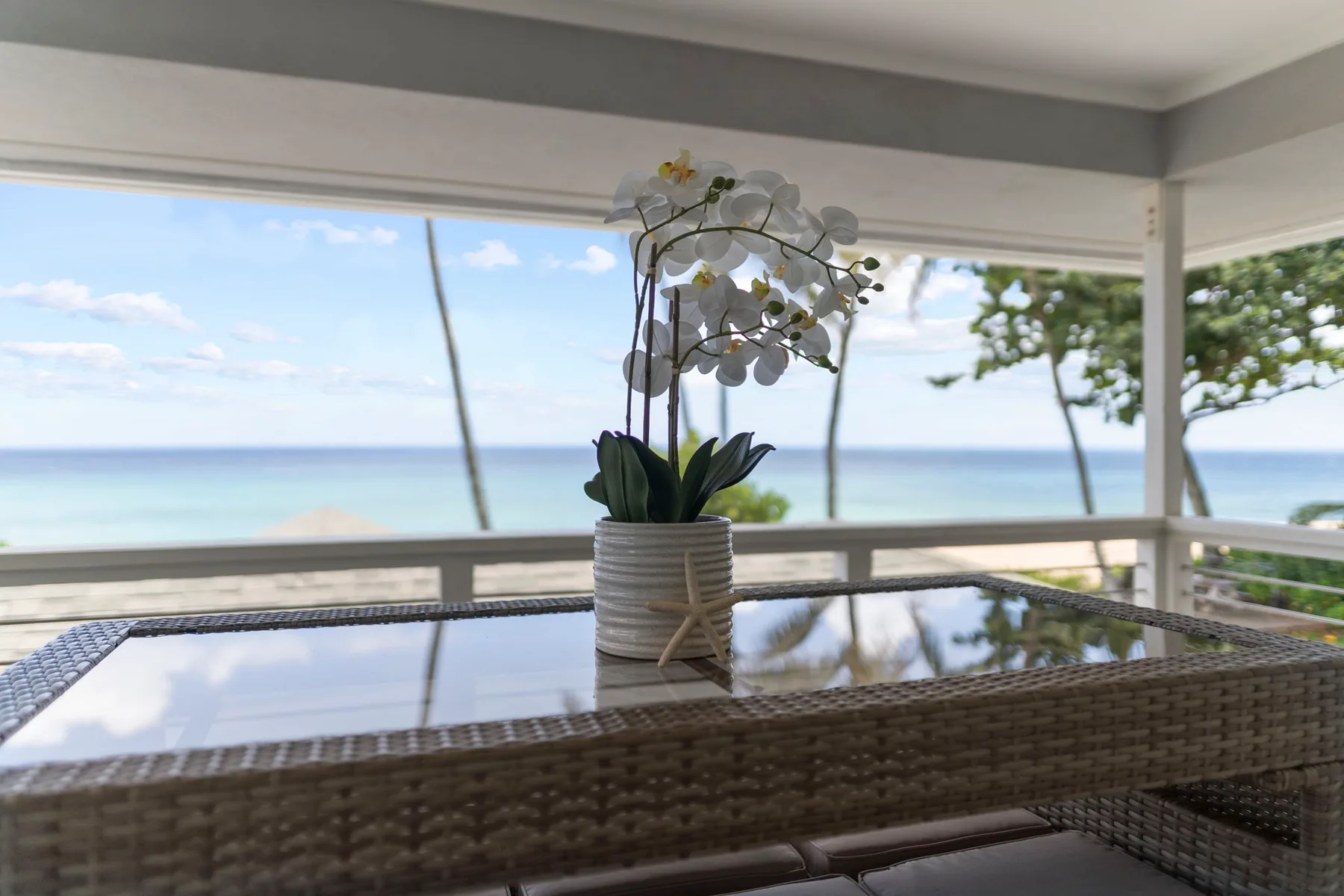 Un patio cubierto tiene una mesa con tapa de vidrio frente al mar.