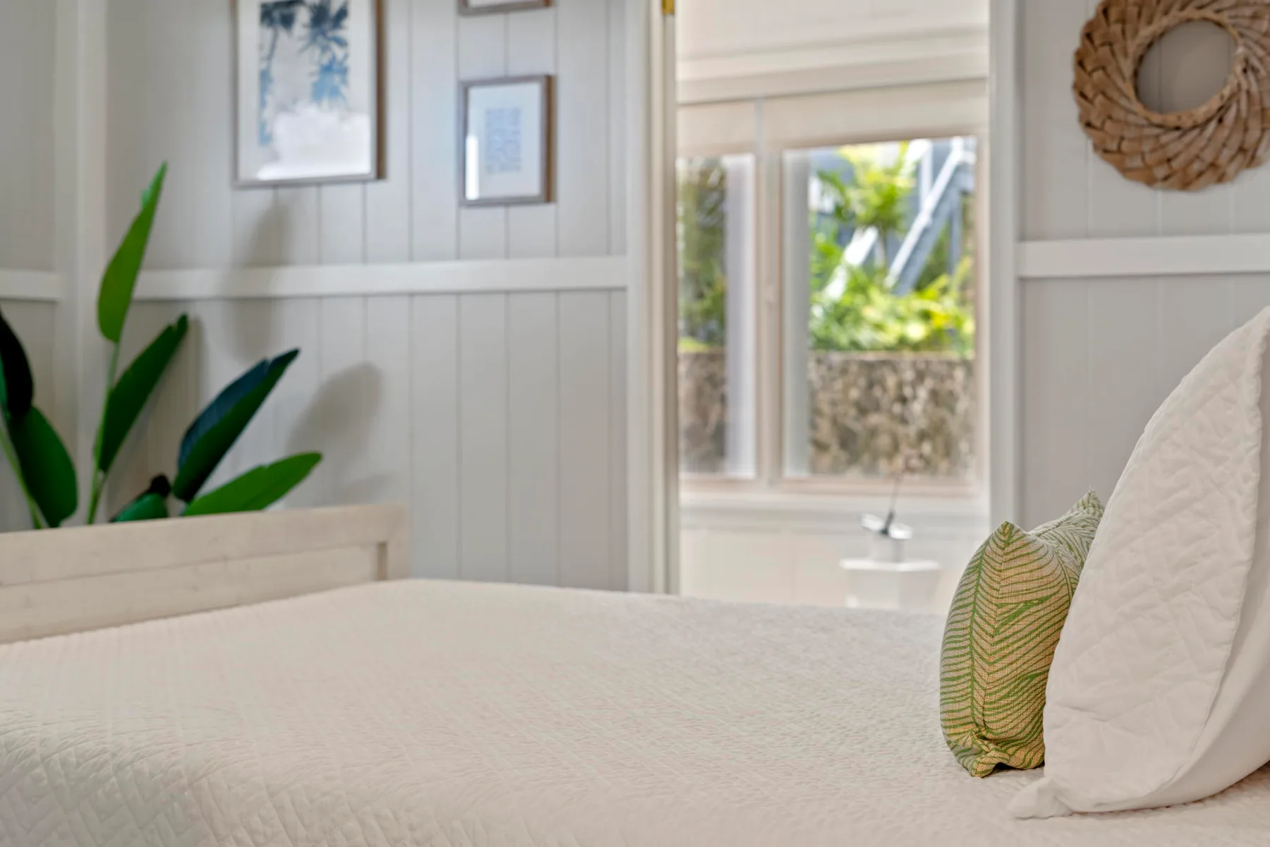 Un dormitorio luminoso con una cama bien tendida y una ventana con vistas a la vegetación.