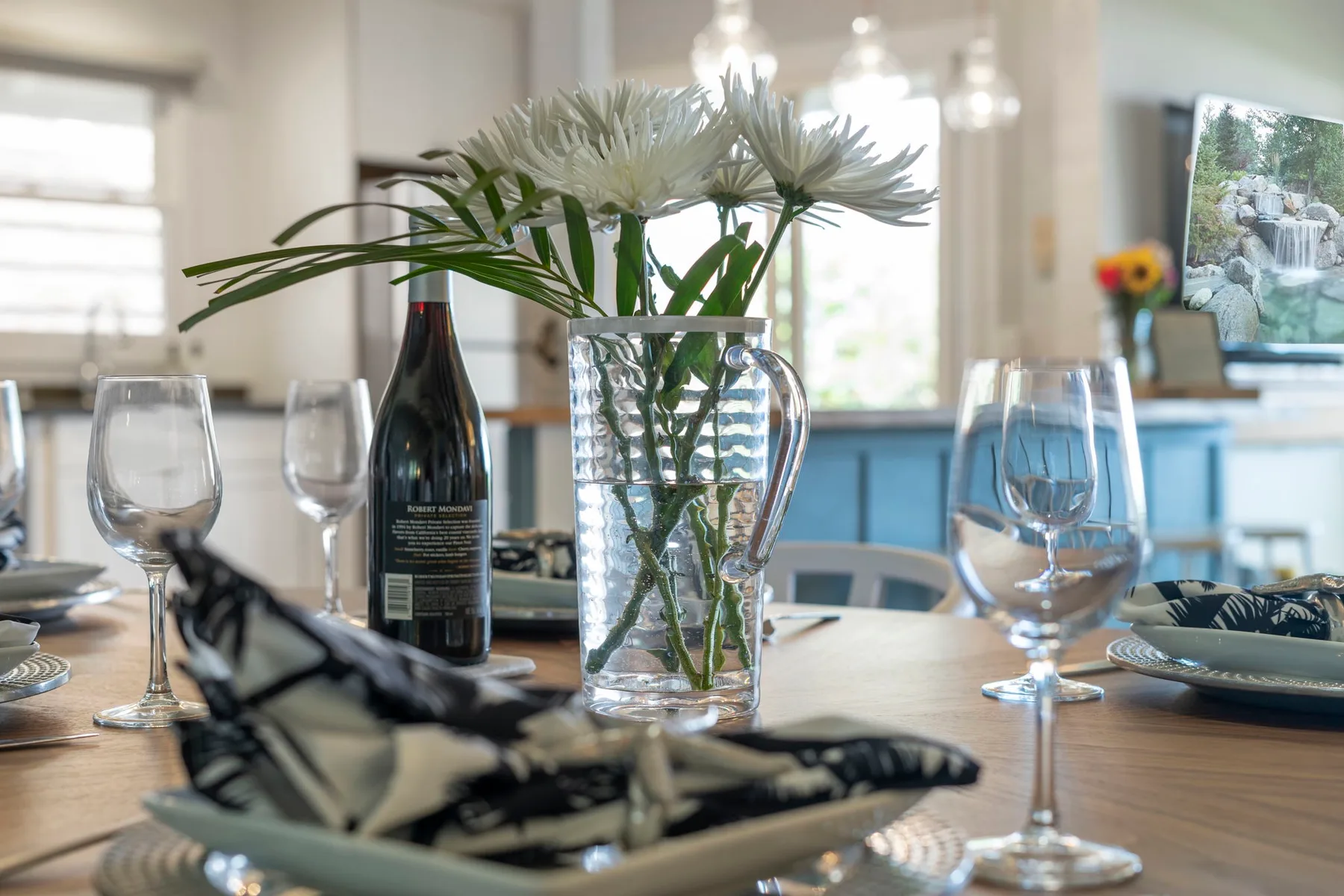 Una mesa de comedor con flores, vino y cubiertos está en una cocina luminosa.