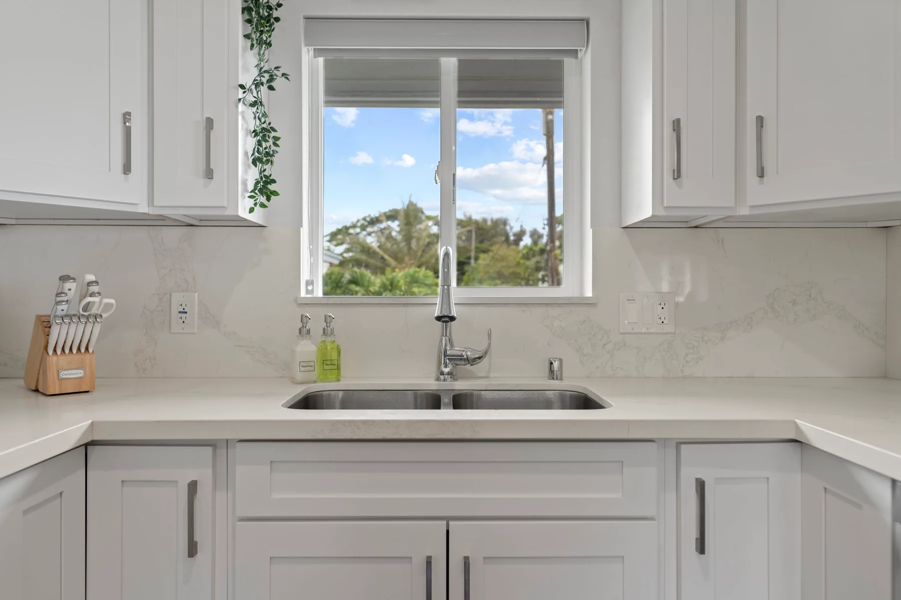 Una cocina blanca y luminosa con un fregadero debajo de una ventana.