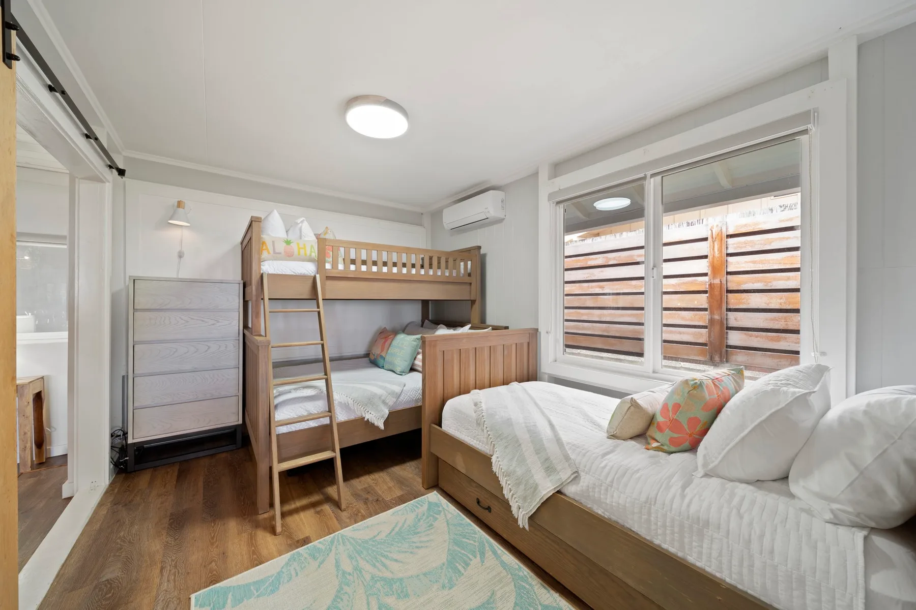 Dormitorio con literas y una cama individual junto a una ventana grande.