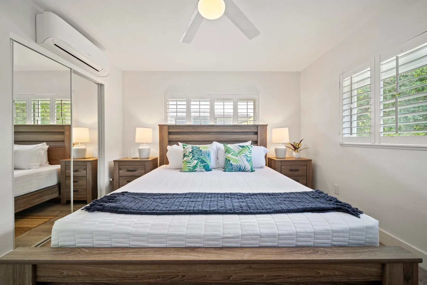 Un dormitorio luminoso con una cama bien tendida y ventanas detrás del cabecero.