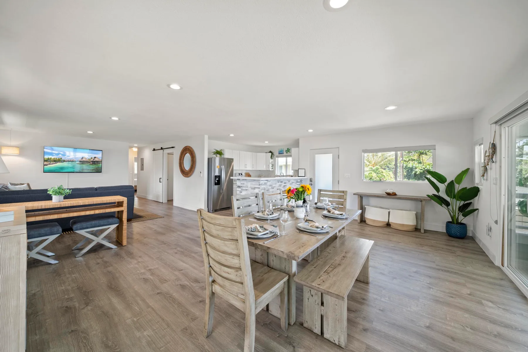 Un espacio abierto de comedor y sala, con una mesa larga de madera y la cocina al fondo.