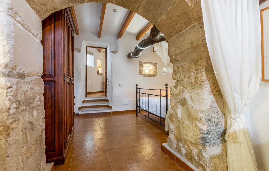 A stone interior passage with tiled flooring, exposed beams, and a metal railing.