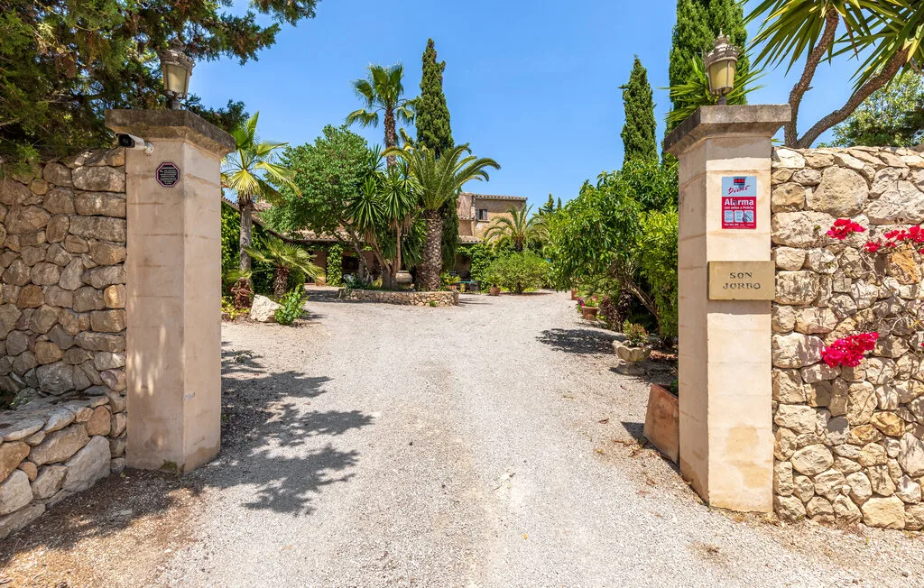A gravel driveway leads through a stone entrance toward a garden.