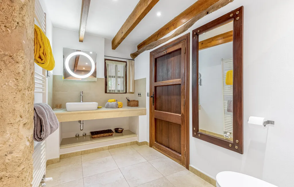 A bathroom with a sink vanity, round mirror, and wooden ceiling beams.