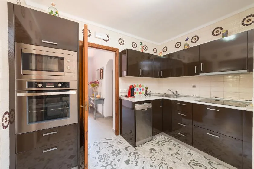 Una cocina moderna con gabinetes oscuros, electrodomésticos empotrados y baldosas estampadas.