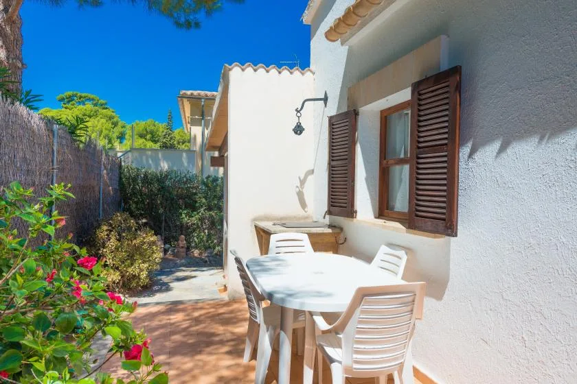 Una zona de comedor al aire libre junto a un edificio blanco, con mesa y asientos.