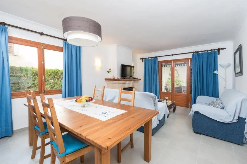 Un comedor con una mesa de madera junto a ventanas con cortinas azules y una zona de estar.