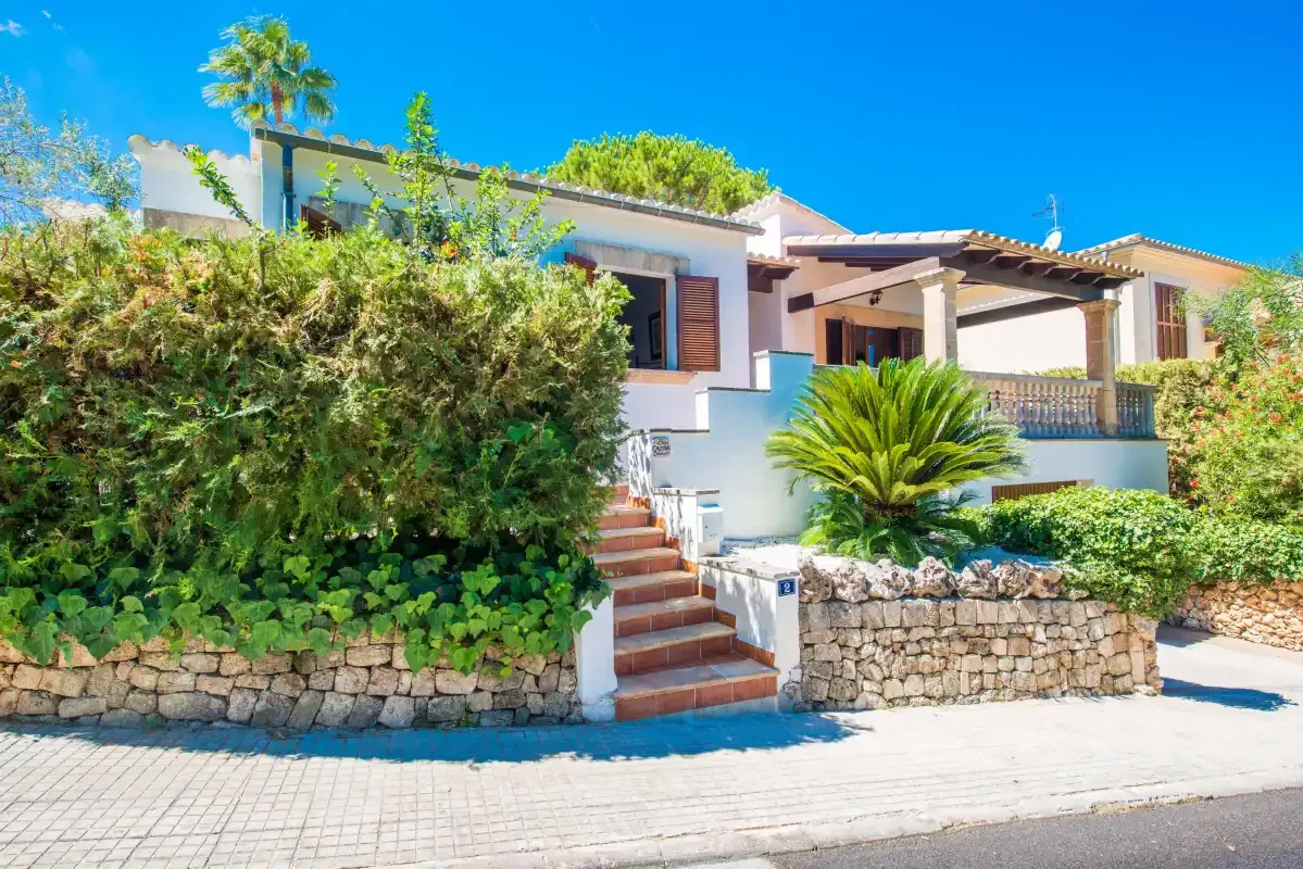 Una casa blanca con una escalera de baldosas terracota y abundantes arbustos.