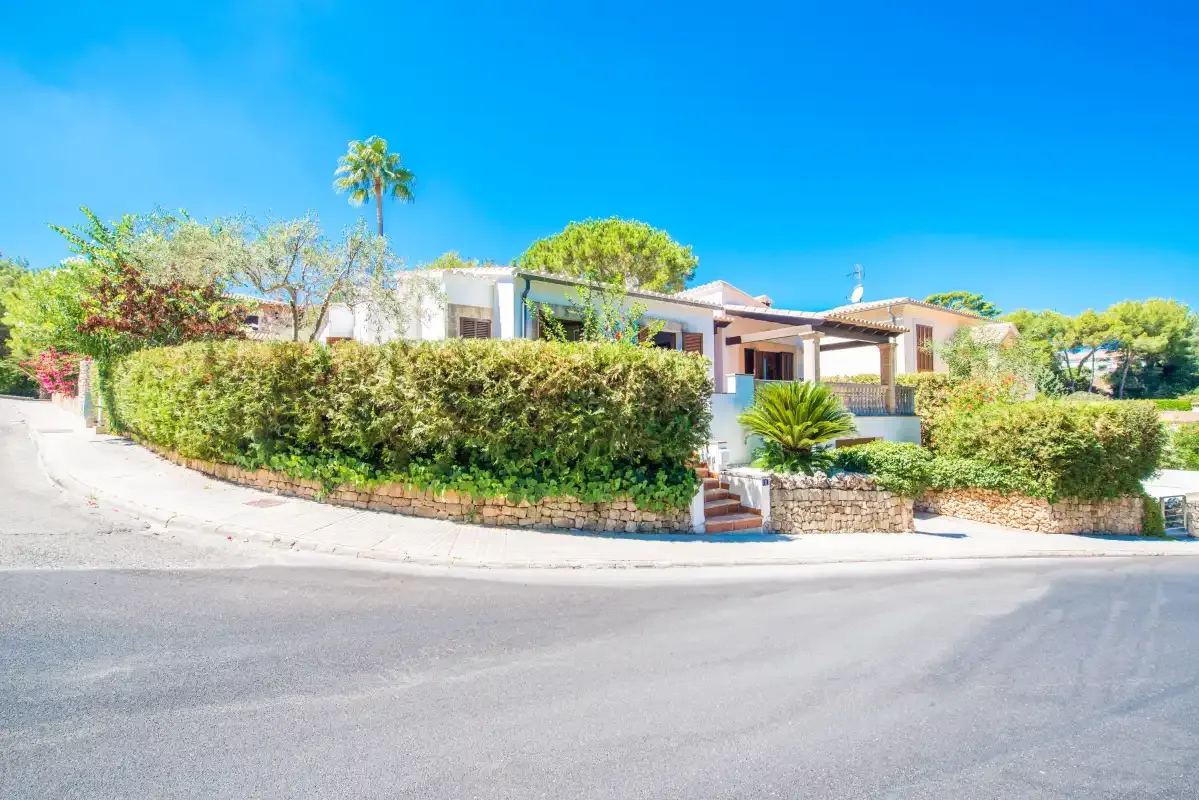 Una casa moderna está detrás de un seto junto a una calle pavimentada curva.