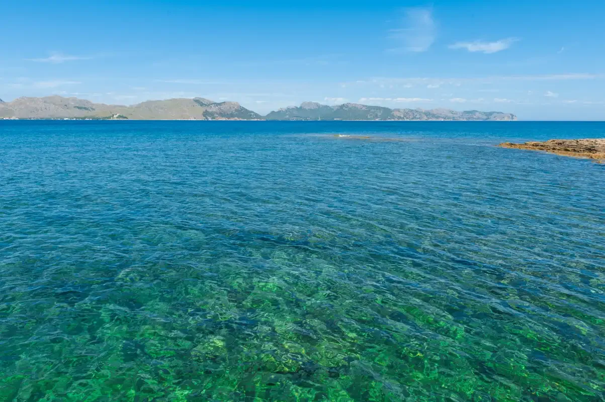 El mar azul y transparente se extiende hacia una costa montañosa.