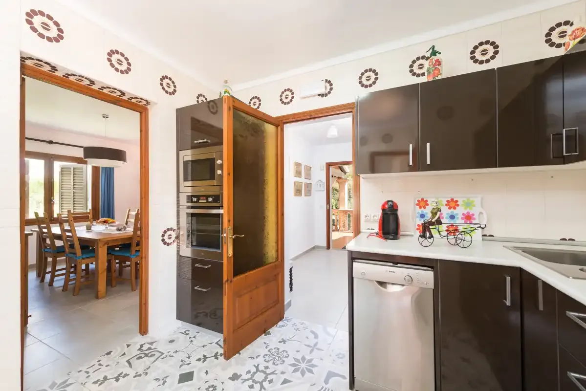 Una cocina con armarios oscuros y una encimera, abierta a un comedor.