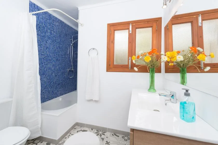 Un baño luminoso con una ducha de azulejos azules y un lavabo blanco.