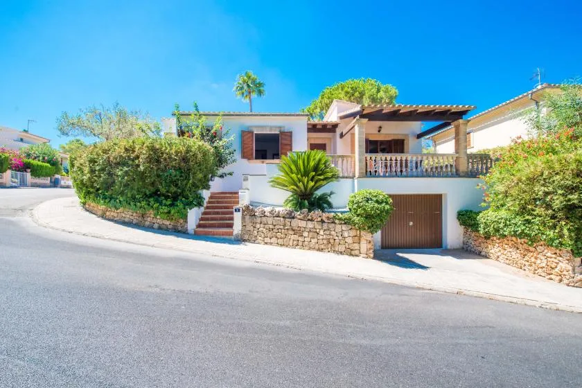 Una casa está junto a una calle curva, con vegetación a lo largo de su muro de piedra.