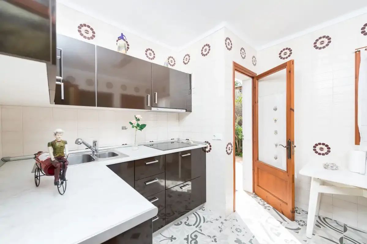 Una cocina luminosa con armarios oscuros, encimeras blancas y una puerta de madera abierta.