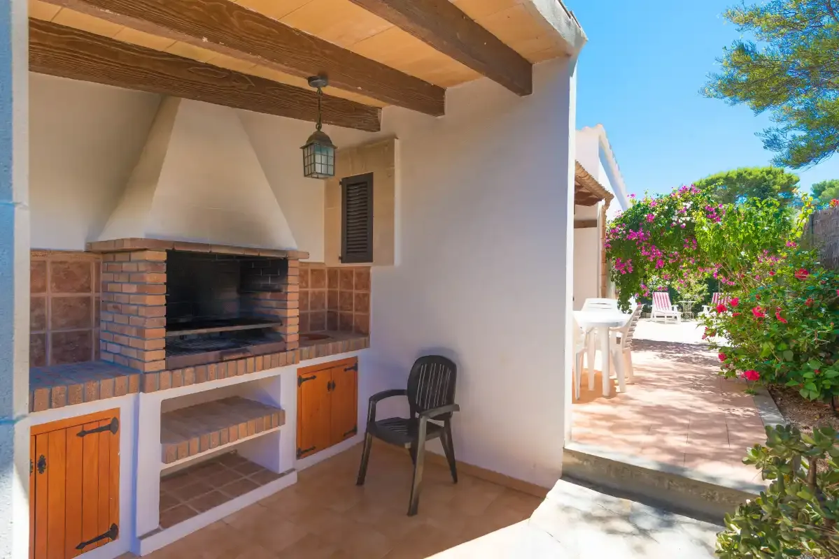 Un patio exterior cubierto con una parrilla empotrada y asientos junto a arbustos floridos.