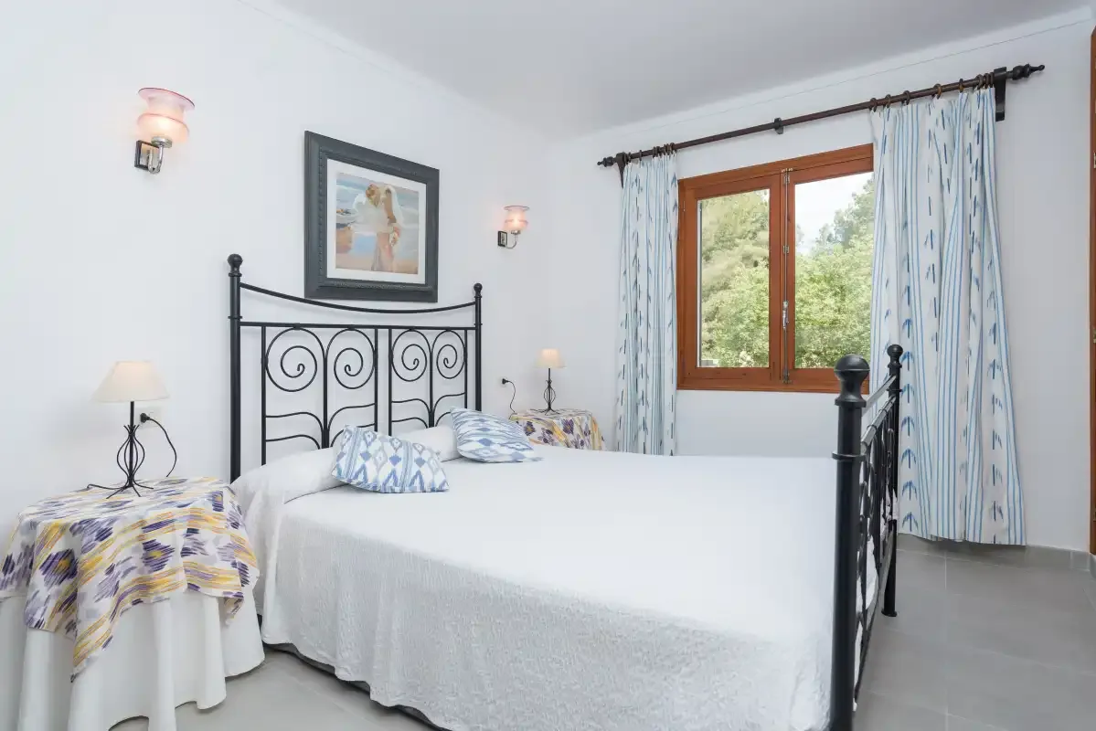Dormitorio con una cama de metal y una ventana con vistas a la vegetación.