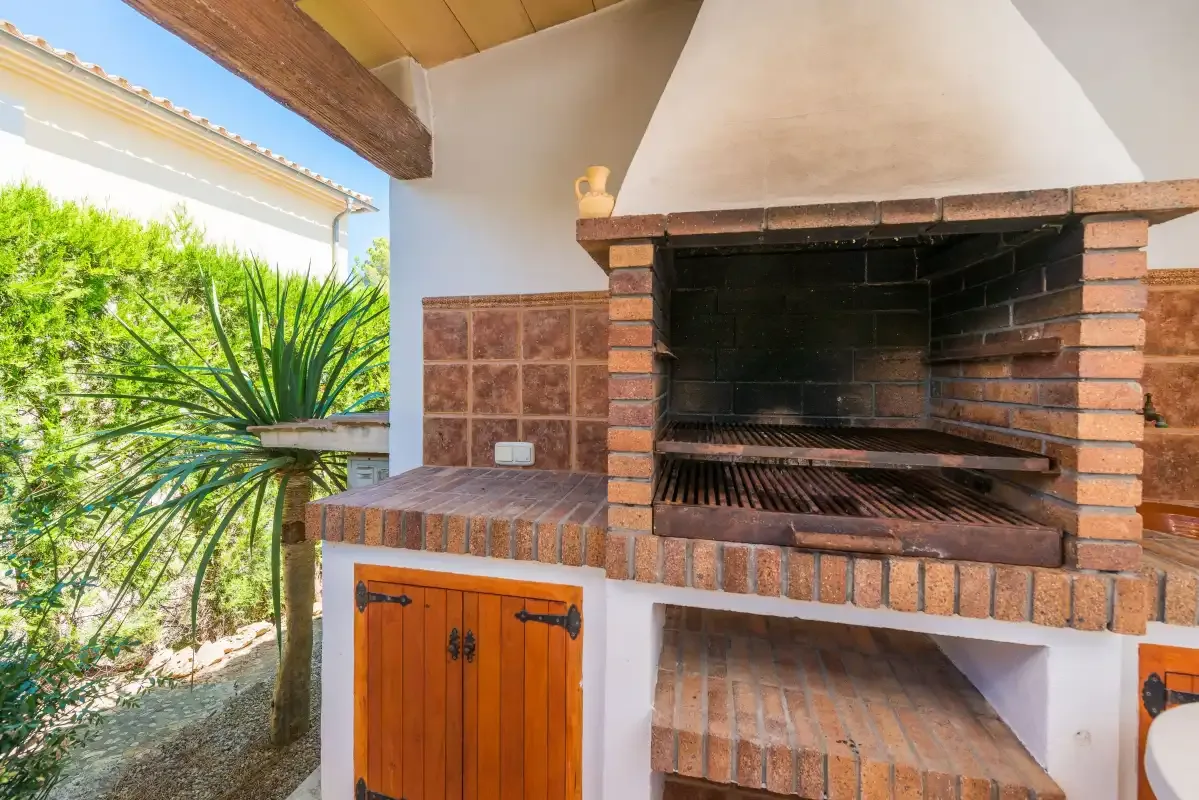 Una zona exterior de barbacoa de ladrillo con una parrilla grande y un armario de madera.