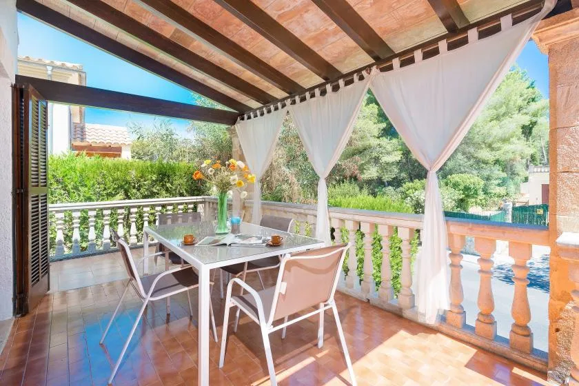 Una terraza cubierta con una mesa de comedor y sillas junto a cortinas blancas.