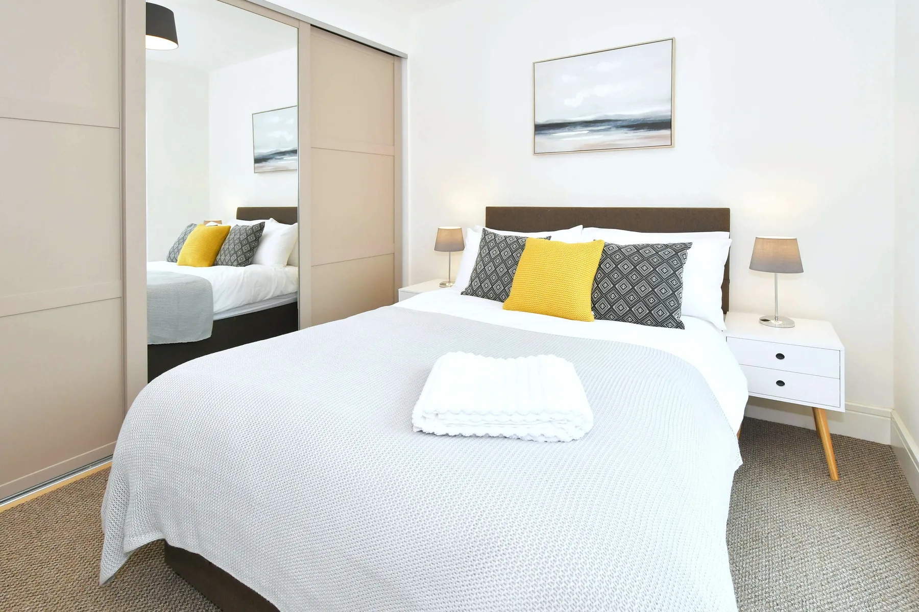 A bright bedroom with a neatly made bed, patterned cushions, and bedside tables.