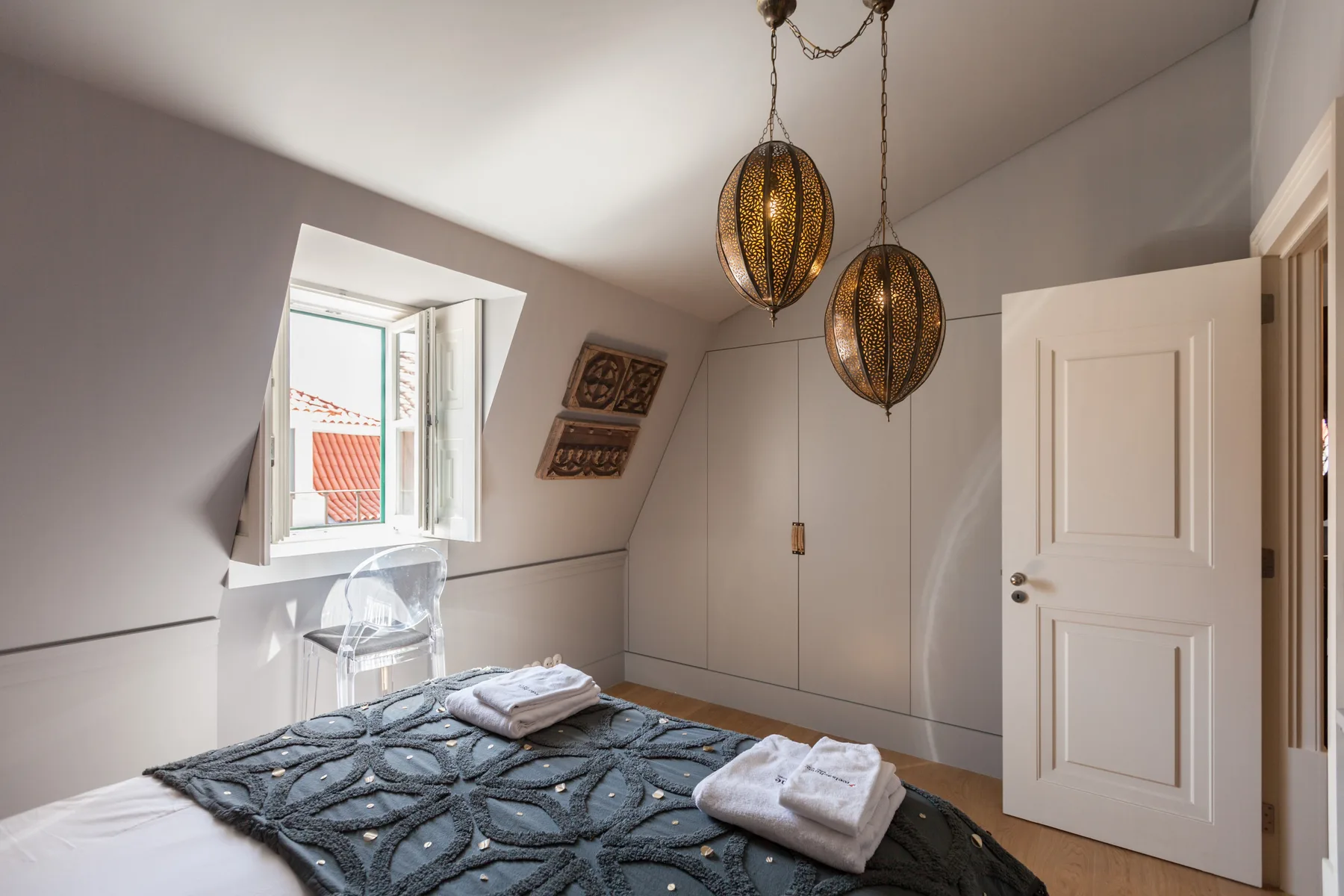 Un dormitorio con una cama, toallas dobladas y dos lámparas colgantes.