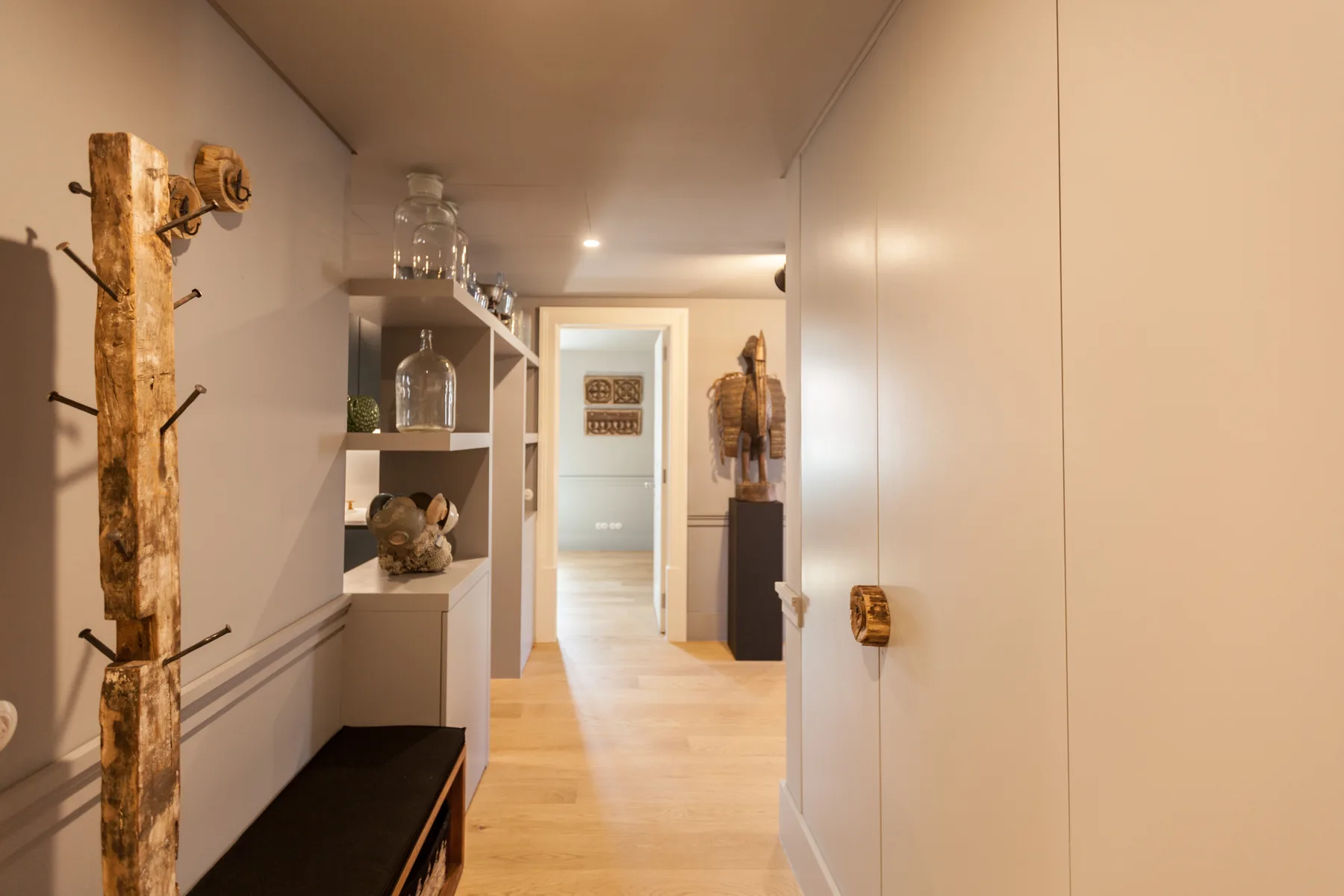 Un pasillo luminoso de apartamento con estantes abiertos y un perchero de madera.