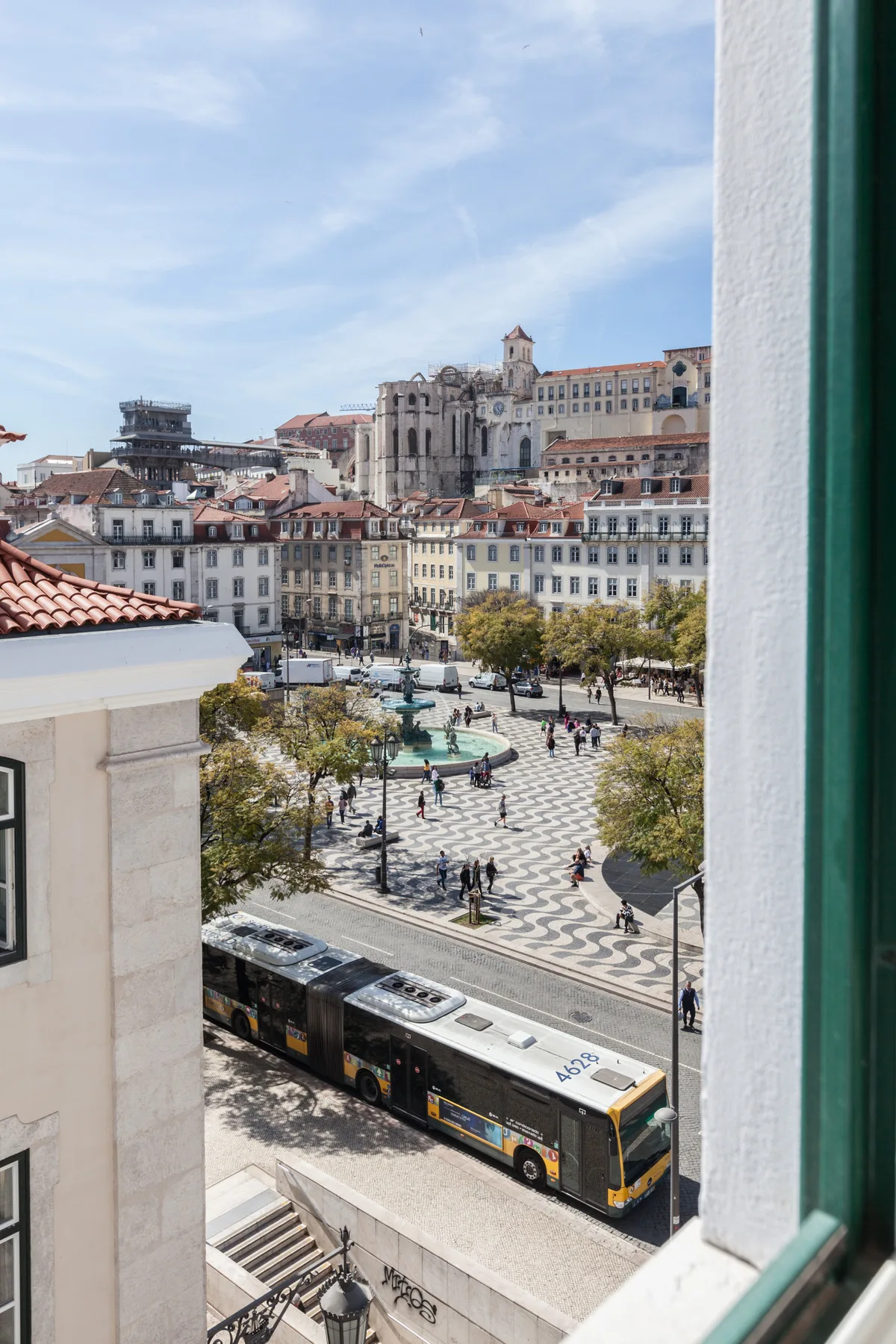 A city square with patterned paving, trees, and a bus in the foreground.
