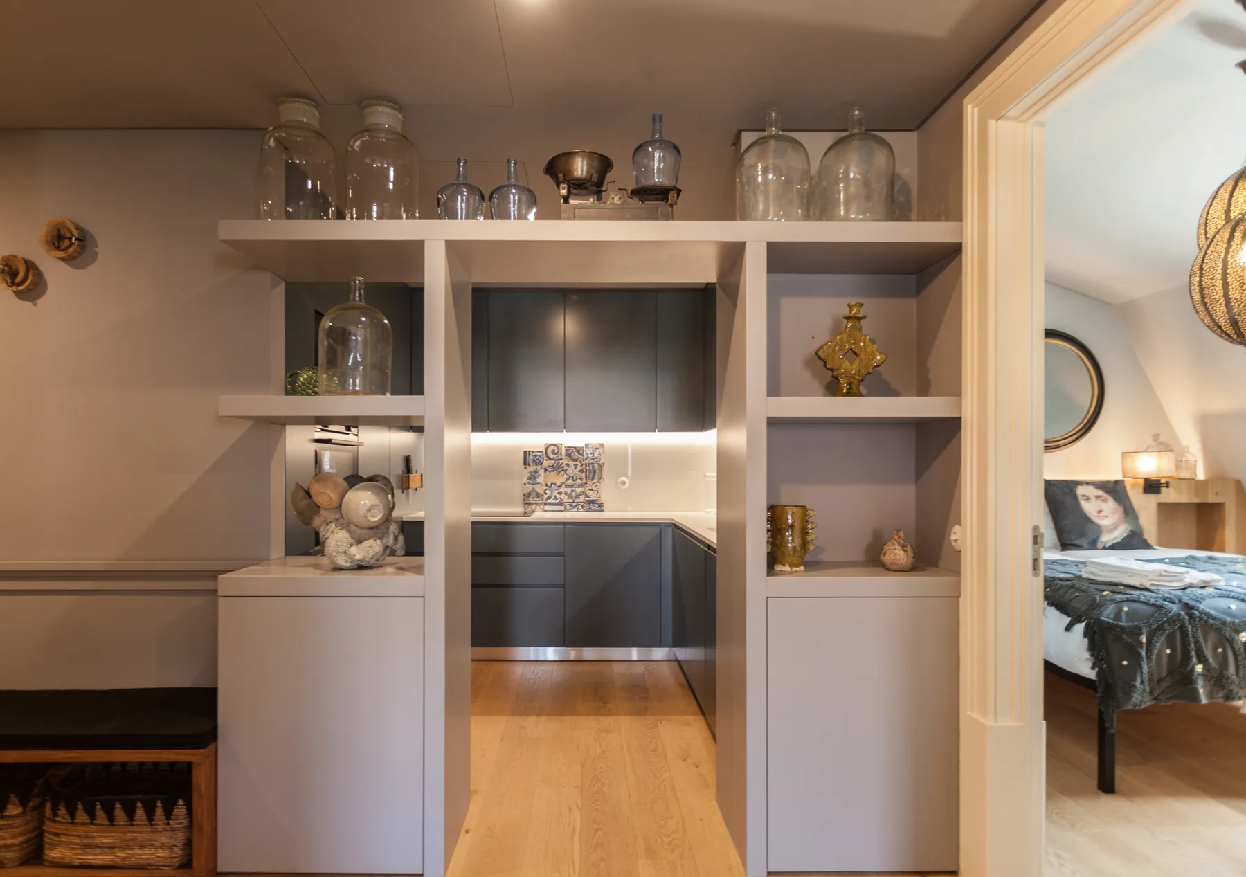 Una estantería empotrada enmarca la vista de una cocina y un dormitorio contiguo.