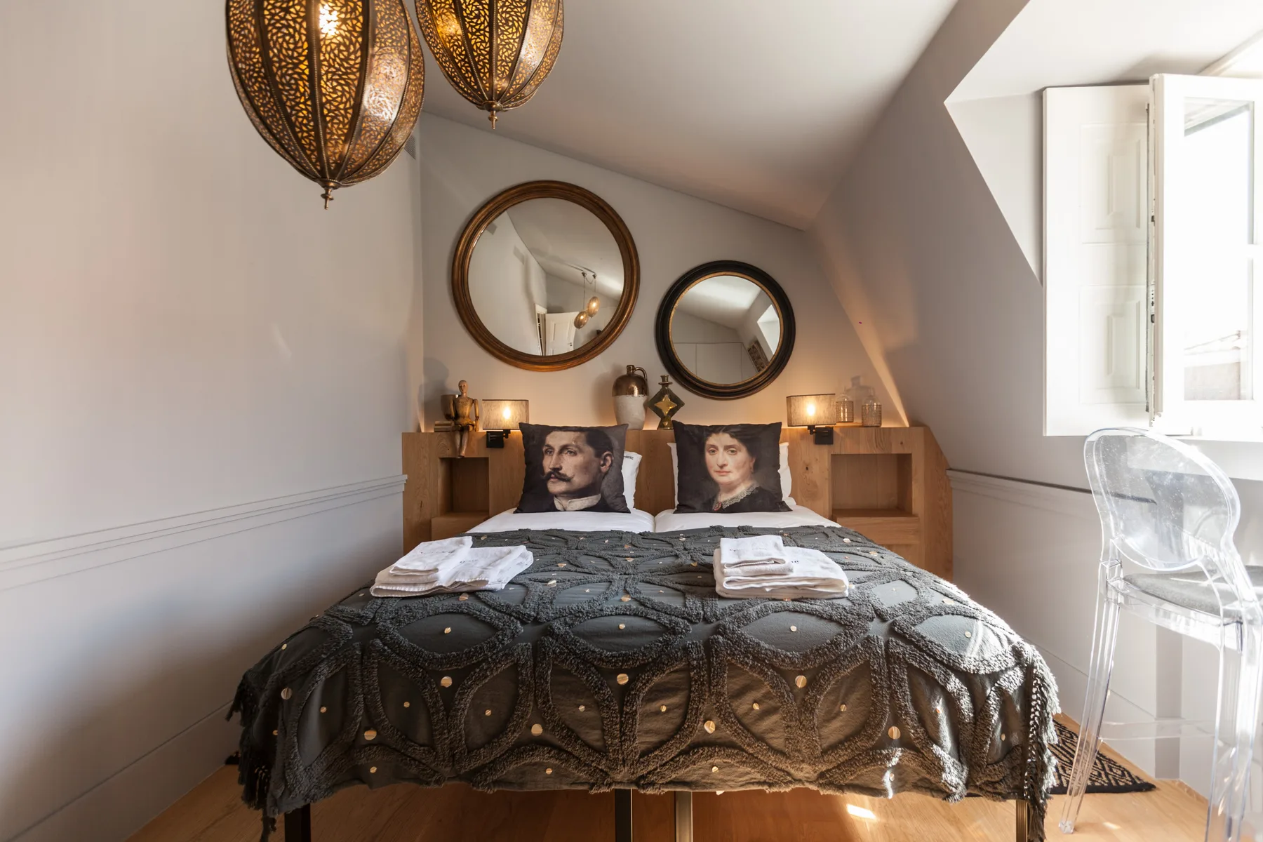 A bedroom with a double bed, decorative mirrors, and an open window.