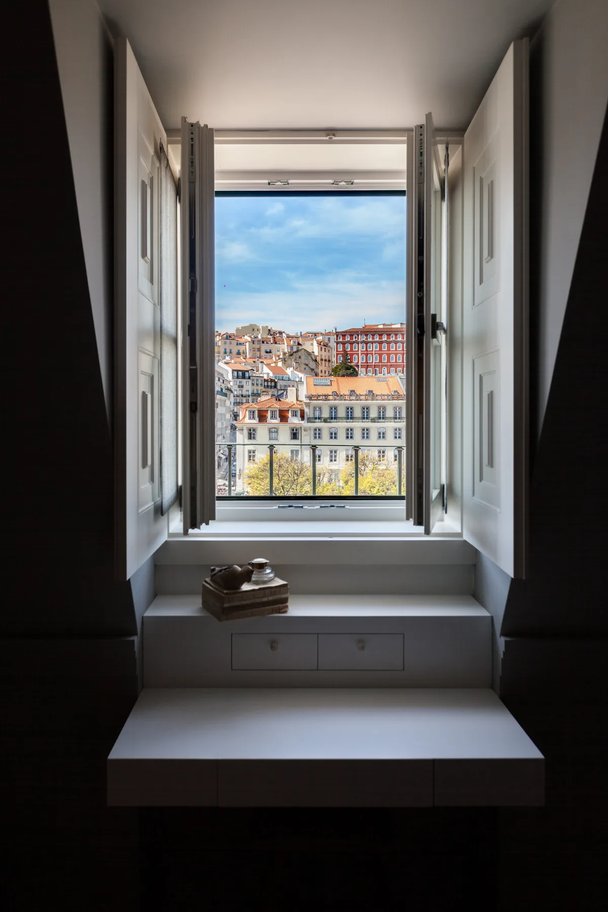 Un rincón luminoso junto a la ventana ofrece vistas de tejados de la ciudad bajo un cielo azul.