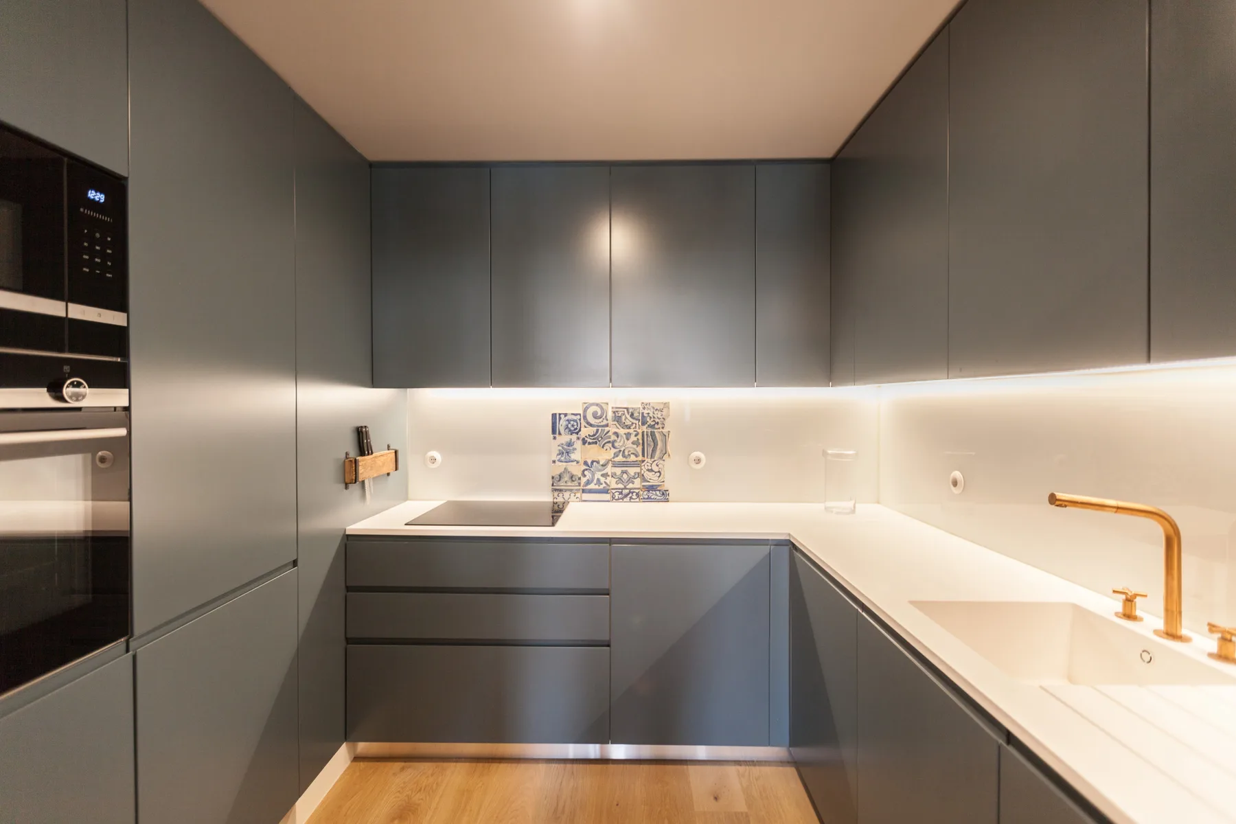 Una cocina moderna con gabinetes grises, encimeras blancas y horno empotrado.
