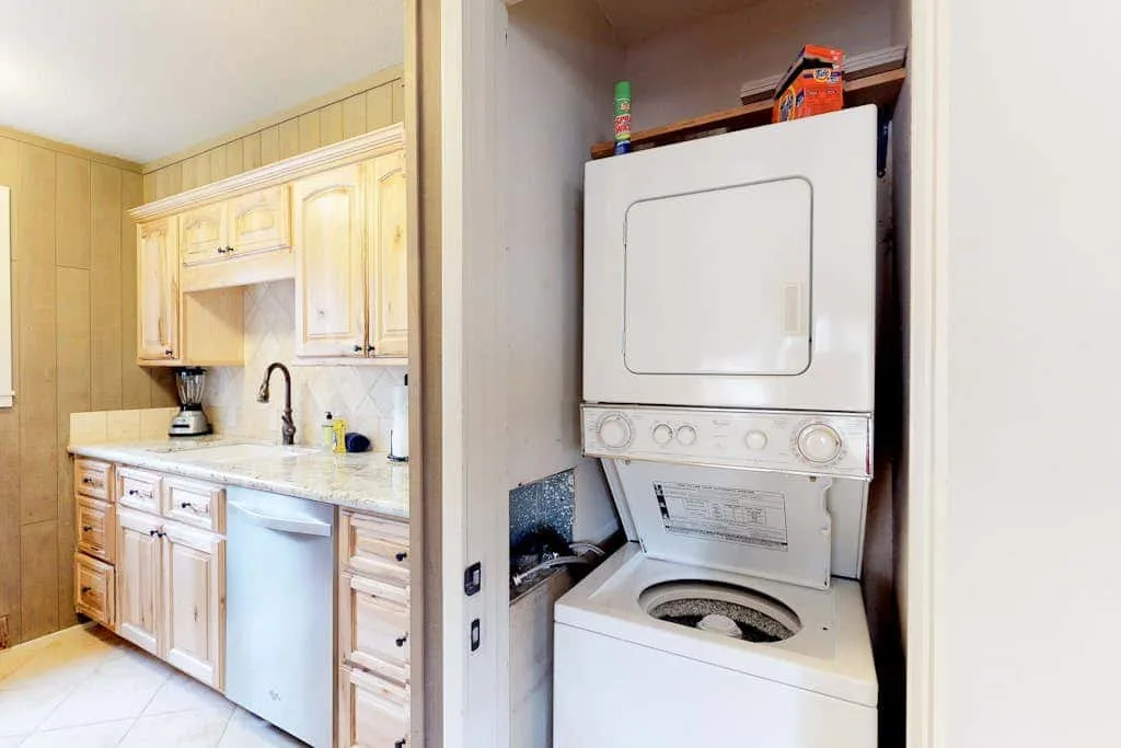 Una cocina con gabinetes de madera y fregadero junto a un área de lavado con lavadora y secadora apiladas.