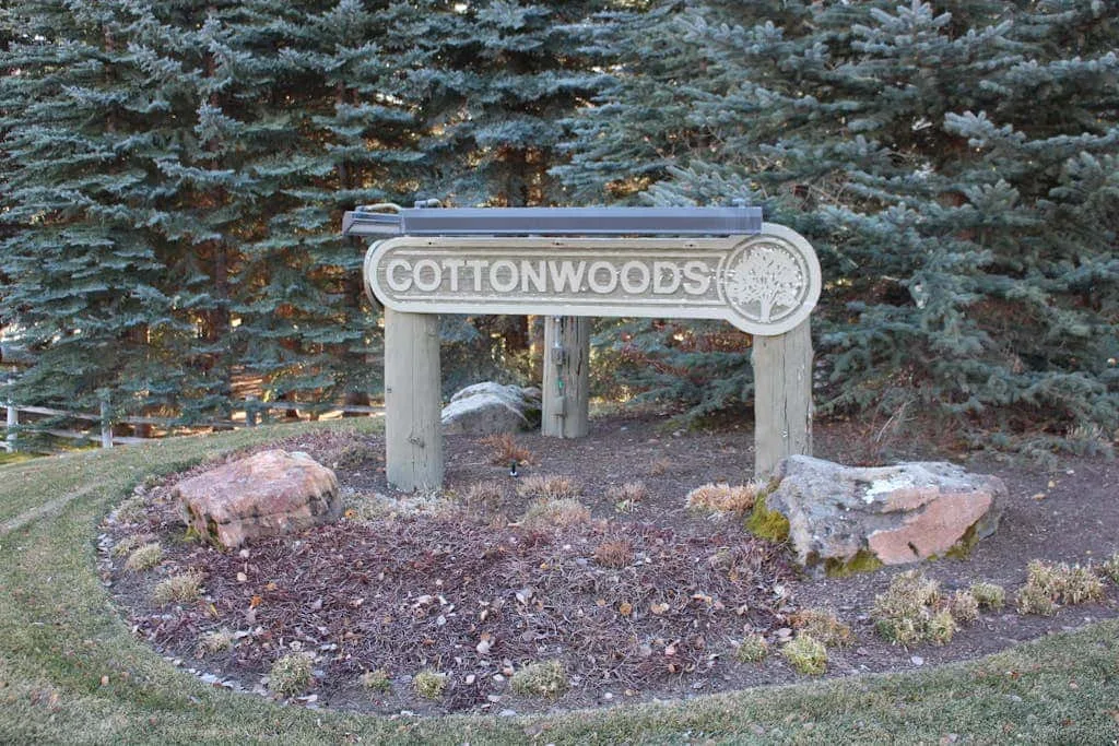 Un letrero de madera que dice «Cottonwoods» está en un jardín ajardinado entre árboles de hoja perenne.