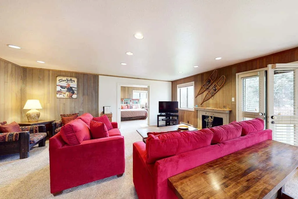 Una sala de estar con asientos rojos, una mesa de madera y una chimenea.