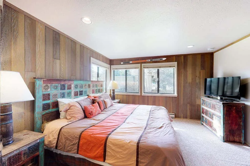 Un dormitorio con una cama, paredes revestidas de madera y ventanas.