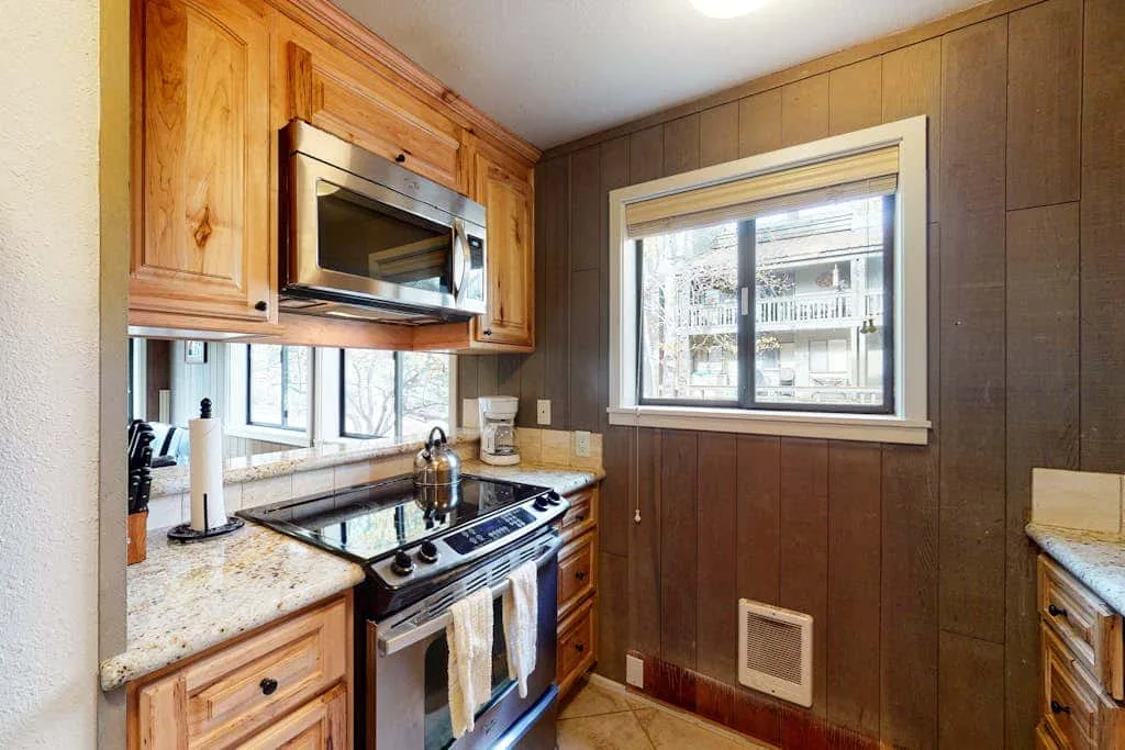 Una cocina con gabinetes de madera, una estufa y ventanas.